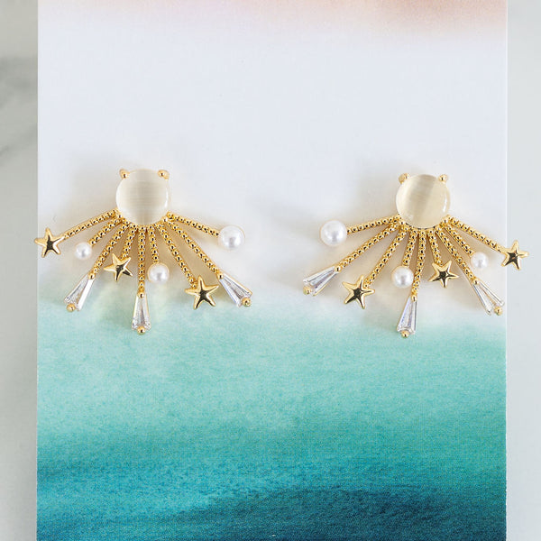 Picture of starburst golden earrings. Earrings have large white bead at their center and small pearls, small gold stars and small diamonds at the end of the starburst.