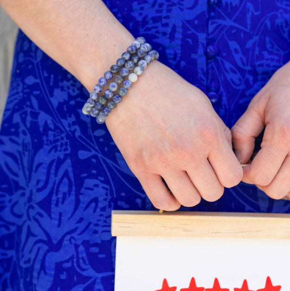 Picture of model's wrist with a set of three blue and gray marbled beaded bracelets.