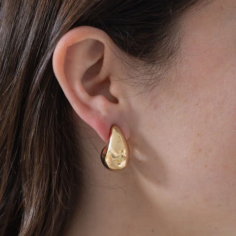 Model wearing a chunky gold teardrop earring.