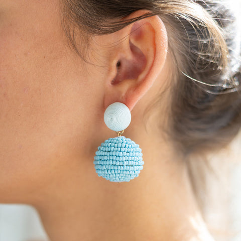 Woman wearing dangly bauble earrings with a light blue circle and a bigger dark blue circle attached to it