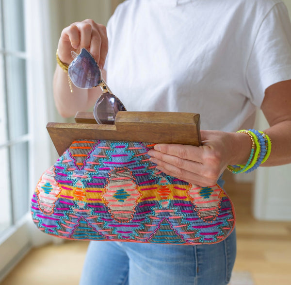 Person putting sunglasses in a clutch with brown at the top and a purple, orange, and yellow colored cloth design 