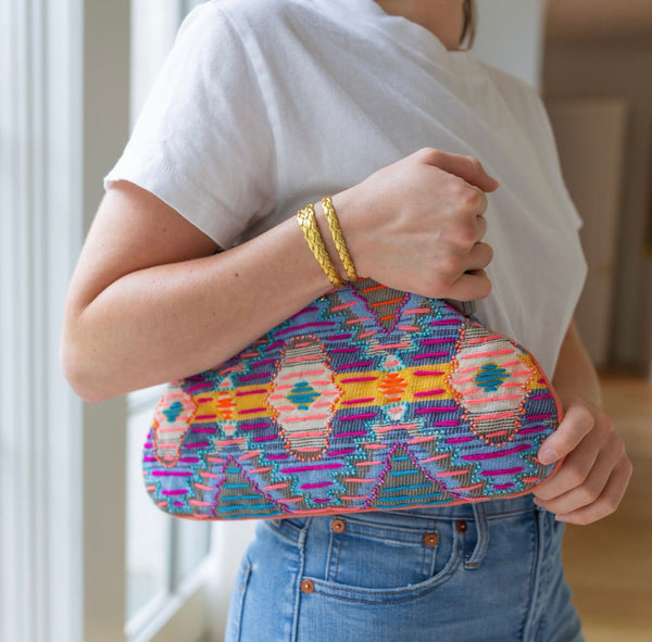 Person holding in their arms a clutch with brown at the top and a purple, orange, and yellow colored cloth design 