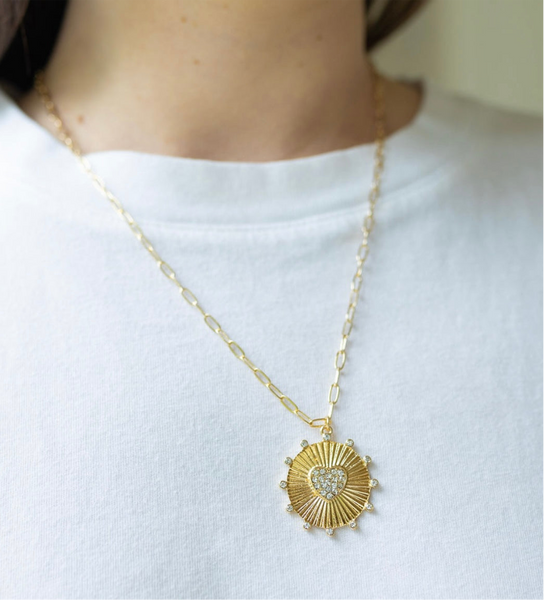 Girl wearing a necklace around her neck with a gold thin chain with a sun/heart medallion attached to it