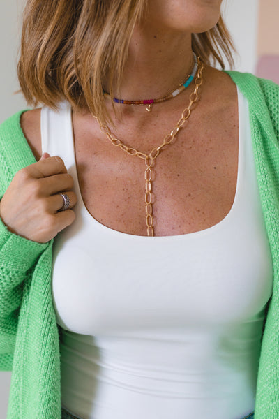 Woman wearing a gold toggle chain necklace with a small beaded rainbow-colored necklace