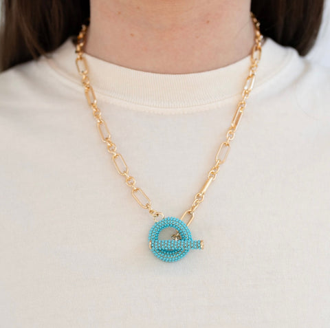 Model wearing a gold toggle chain with turquoise beaded toggle.