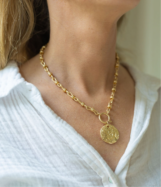 Woman wearing a gold chunky chained necklace with a large gold medallion attached to it