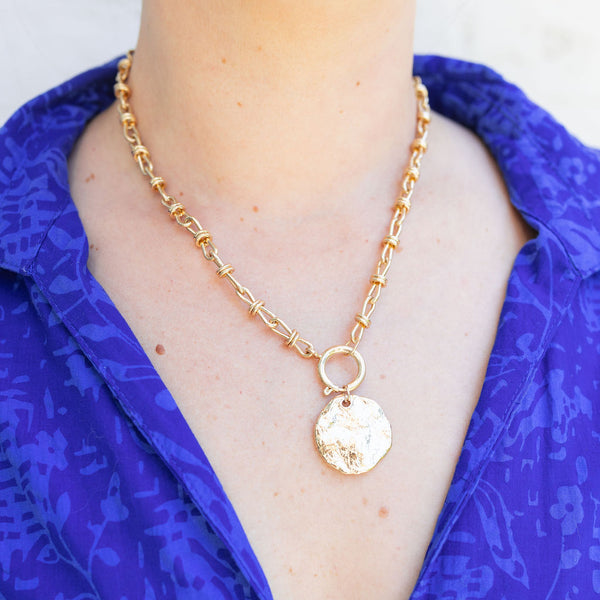 Woman wearing a gold chain necklace with a gold circular piece attached to it