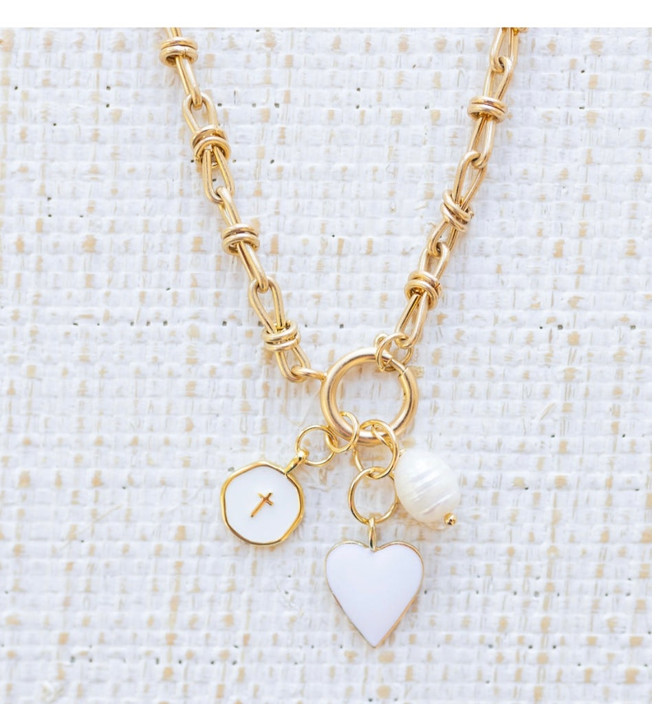 Picture of gold toggle chain with a white heart charm, white disc charm with a cross at the center and a fresh water pearl charm.