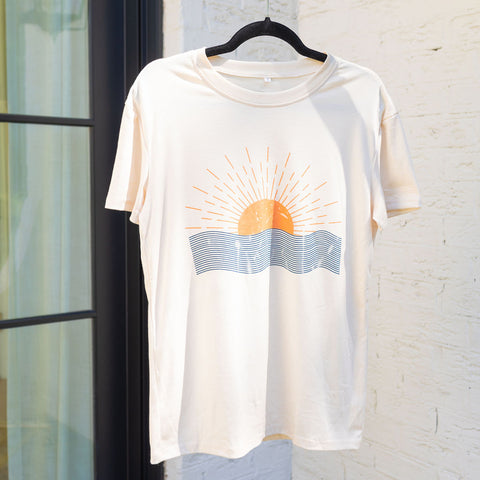 A plain white shirt with an image of an orange sun rising over an ocean 