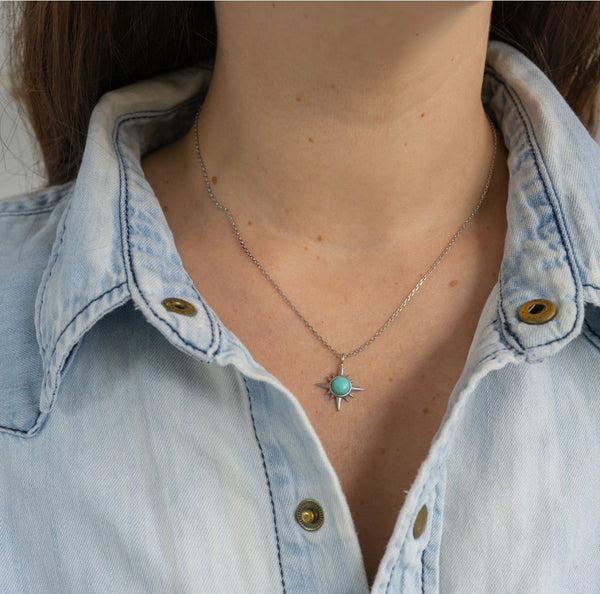 Woman wearing around her neck a gold dainty necklace with a turquoise gemstone attached to it 