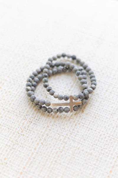 An image of a gray bracelet stack with a gold cross