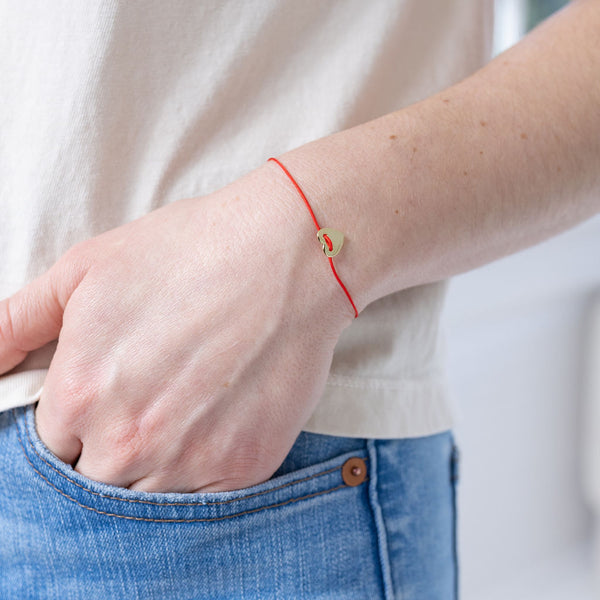 Picture of dainty single strand red string bracelet with small heart pendant.