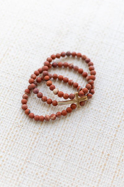 An image of a dark orange bracelet stack with a gold cross