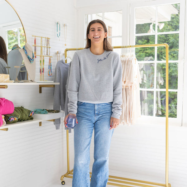 Woman in a house wearing a gray sweater and blue jeans posing and smiling