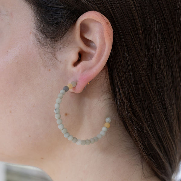 Model wearing hoops covered in matte white, gray and yellow beads.