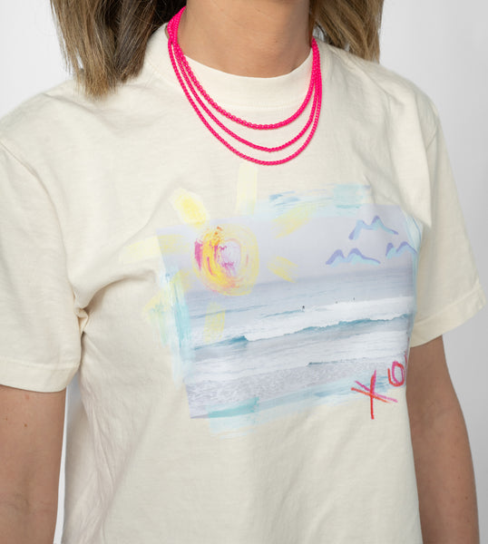 Screenshot of a woman wearing a t shirt displaying a beach scene and wearing bright pink beaded necklaces.