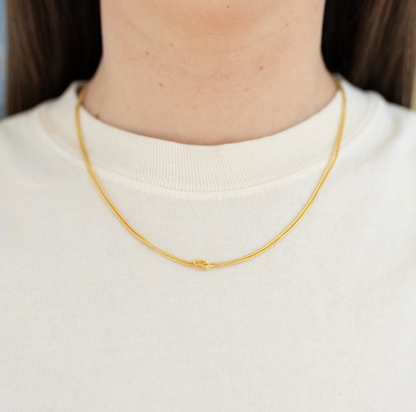 Picture of model wearing a fine gold chain with a knot at its center.