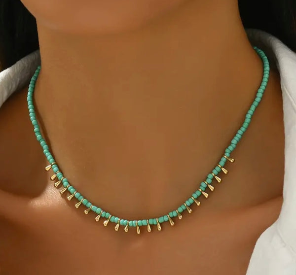 Picture of model wearing a small turquoise beaded necklace with tiny gold dangling beads at the front.