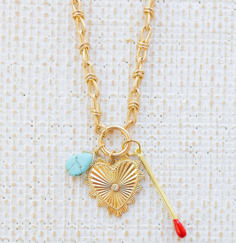 Picture of gold toggle chain with a turquoise teardrop, a large gold heart pendant with a diamond center and a gold matchstick.