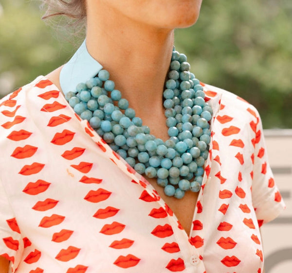 Woman outside wearing a white dress with a red lips print and a big blue stone layered necklace around her neck