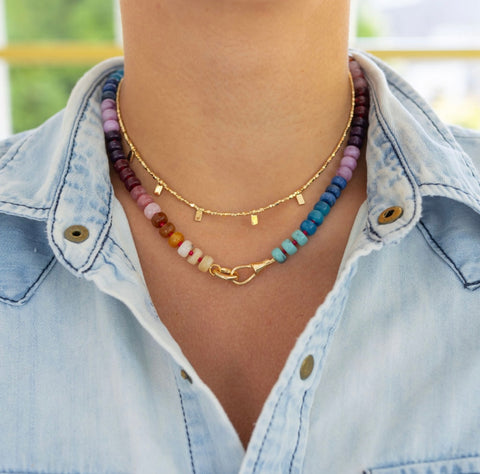 Woman wearing a rainbow colored beaded short necklace and a dainty gold short necklace around her neck