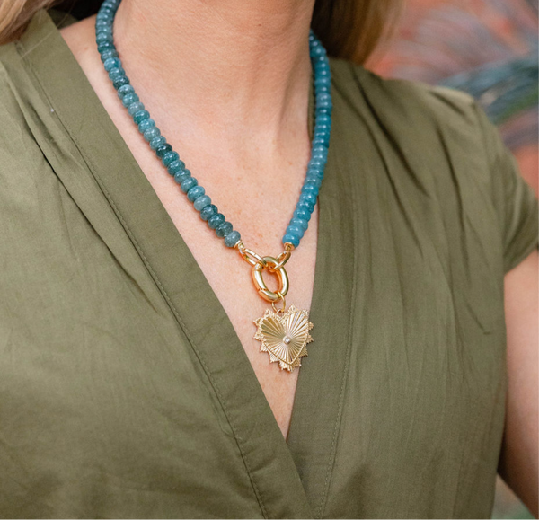 Picture of model wearing a a turquoise beaded necklace with a chunky gold link and large gold heart shaped pendant with a diamond at it's center.