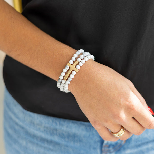 Woman wearing a white gemstone bracelet stack with a gold cross on her wrist