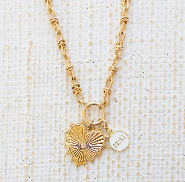 Picture of gold toggle chain with a large gold heart pendant with diamond in the center. Necklace has another white pendant that reads "11:11"