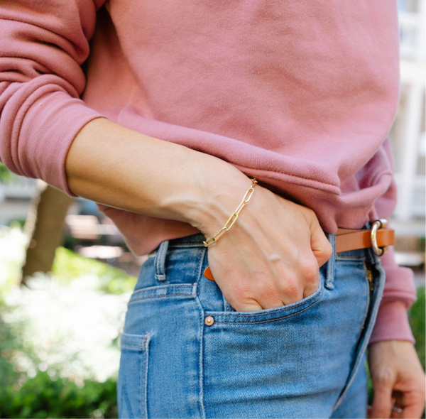 Girl reaching into her front jeans pocket wearing a loose gold chain bracelet on her wrist