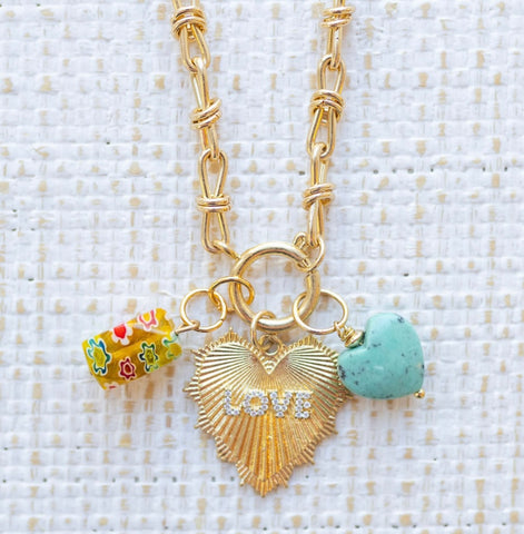 Picture of gold toggle chain with a large gold heart pendant with the word "Love" in diamonds and a yellow flowered charm and blue turquoise heart charm.