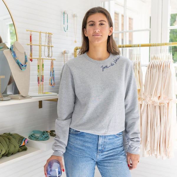 Woman in a house wearing a gray sweater and blue jeans posing and smiling