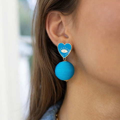 Model wearing blue heart evil eye earring with dangling large blue bead.