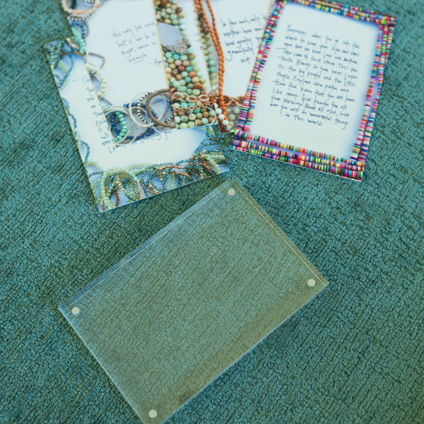 Five affirmation cards with necklaces/beads printed around the border with a clear card sleeve laying on a green surface 