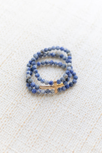 An image of a blue bracelet stack with a gold cross