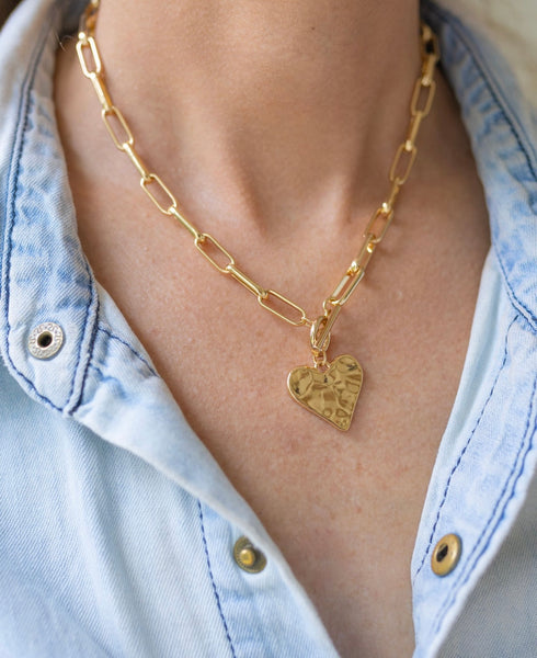 Girl wearing a necklace around her neck with a gold paperclip link chain with a heart medallion attached to it
