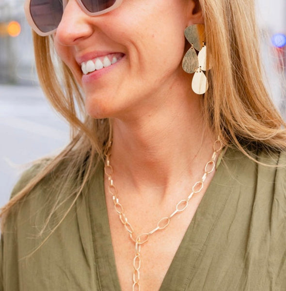 Woman wearing sunglasses looking away smiling wearing a gold four tear dropped dangling earring and a gold chain link necklace